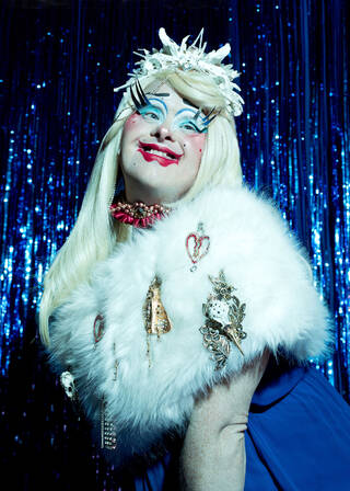 Portrait of Davina Starr, a drag performer with Down's Syndrome, posing in front of a glitter curtain