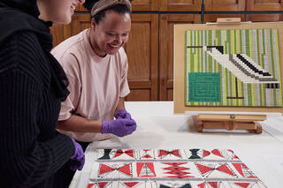 Two people wearing nitrile gloves look at some patterned fabric in a study centre
