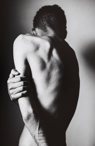 Artist is topless and turns away from the camera