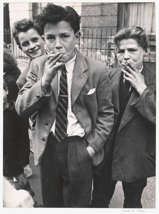 Three teenage boys smoking in the street, wearing blazers and ties