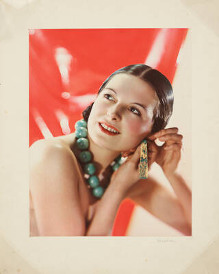 Woman with brown hair and red lipstick, fixing her earring to her ear