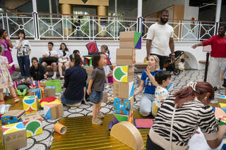 A group of children and adults play with colourful large blocks on a chequered floor